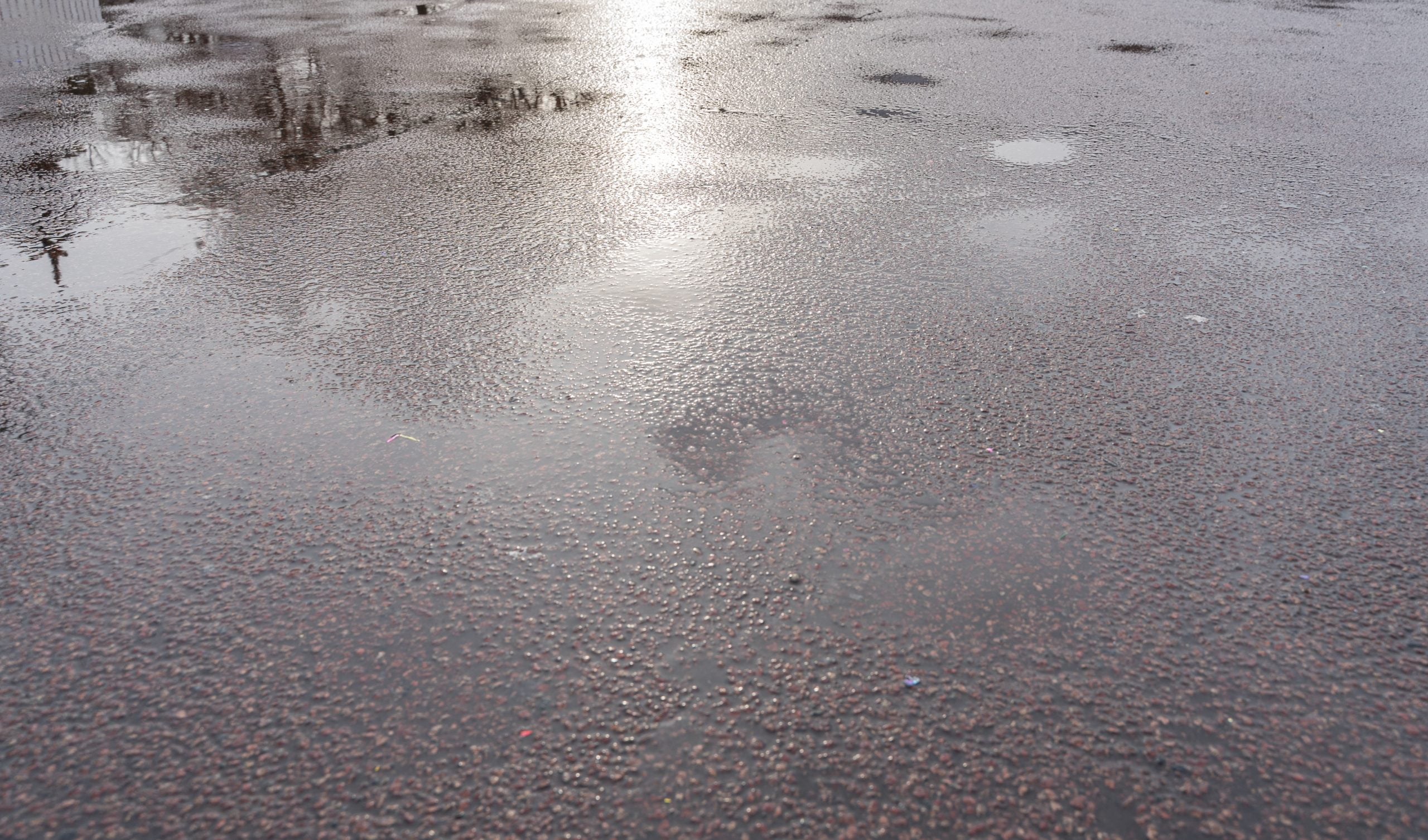 wet asphalt. gray coarse fabric Wet pavement with water reflections and scattered puddles on cloudy asphalt surfaces.