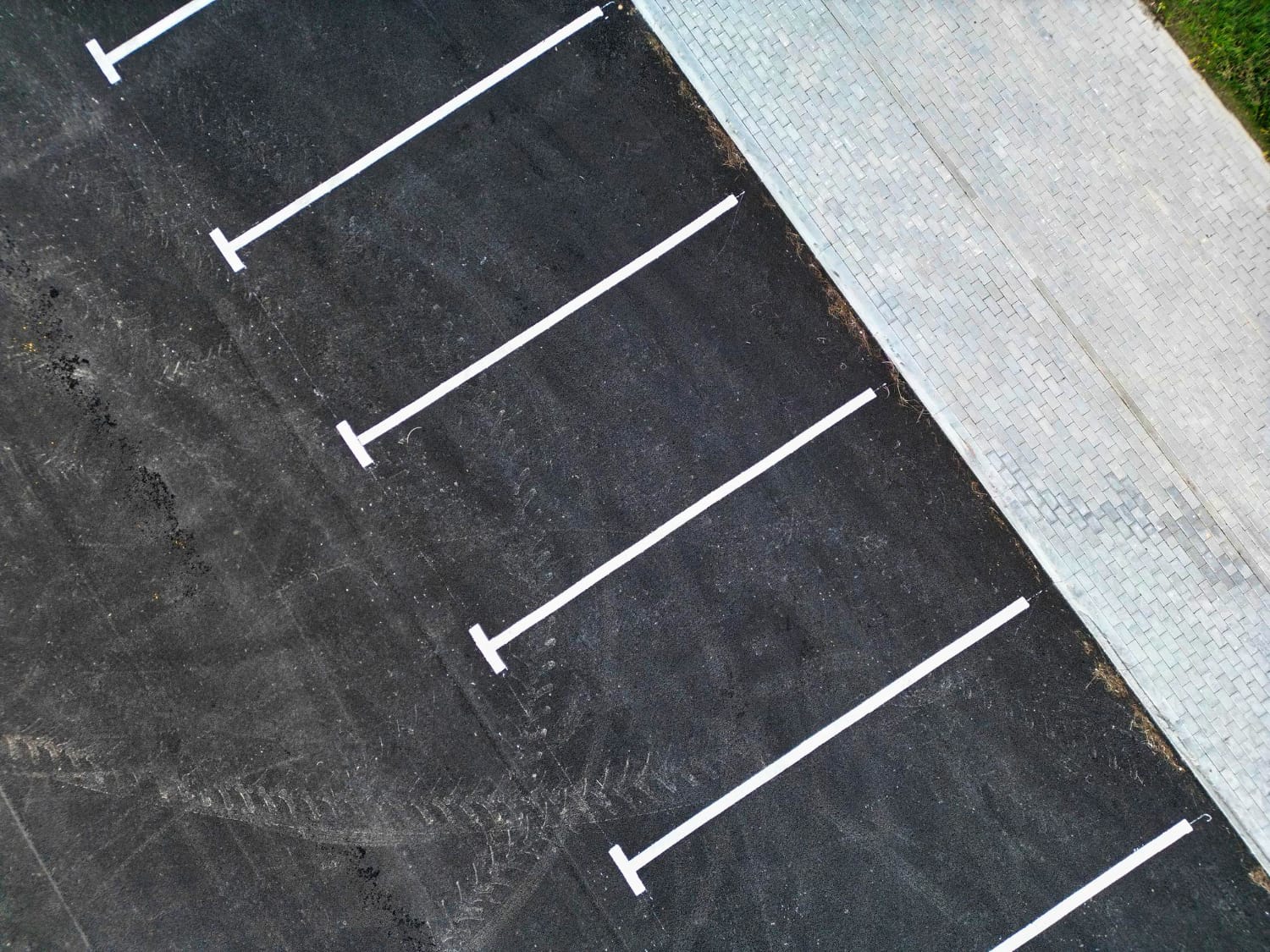 Aerial view of empty parking spaces with white lines next to a paved sidewalk.