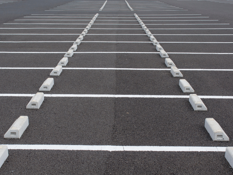 An empty asphalt parking lot with white lines and concrete wheel stops in neat rows.