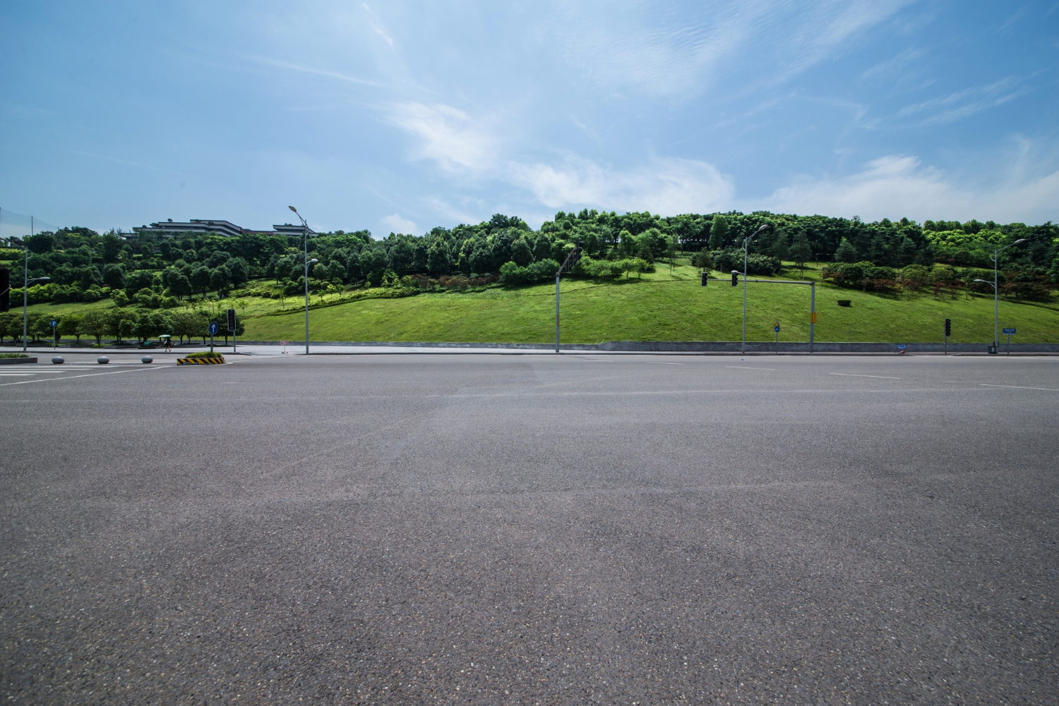 1840 Wide empty road with a grassy hill and trees in the background under a partly cloudy blue sky.